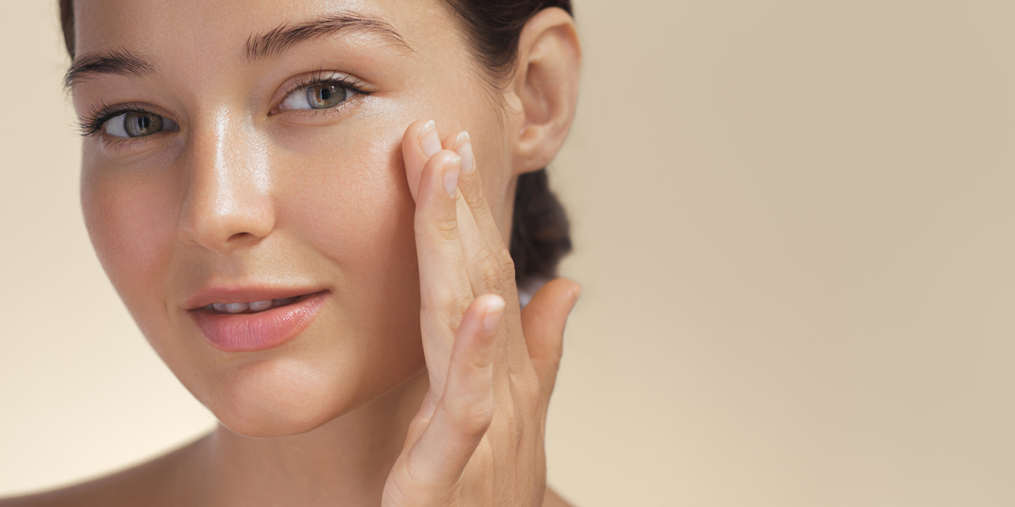 Skincare. Woman with beautiful face touching healthy facial skin portrait. Beautiful smiling Asian girl model with natural makeup enjoys glowing hydrated skin on beige background closeup.